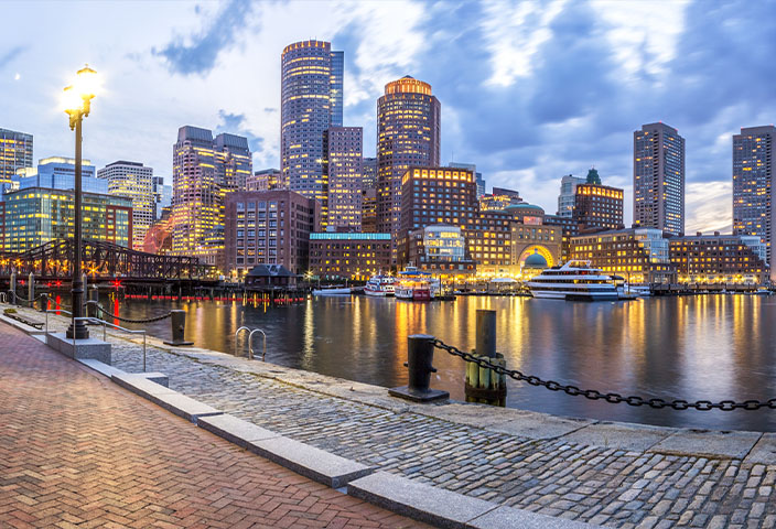 Panoramic view of the Boston skyline and Harbor at twilight, featuring the illuminated Rowes Wharf.