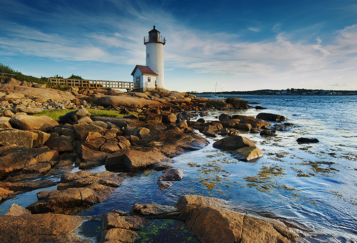 Annisquam Harbor Lighthouse with a wooden walkway on a rocky shoreline in Gloucester, Massachusetts.