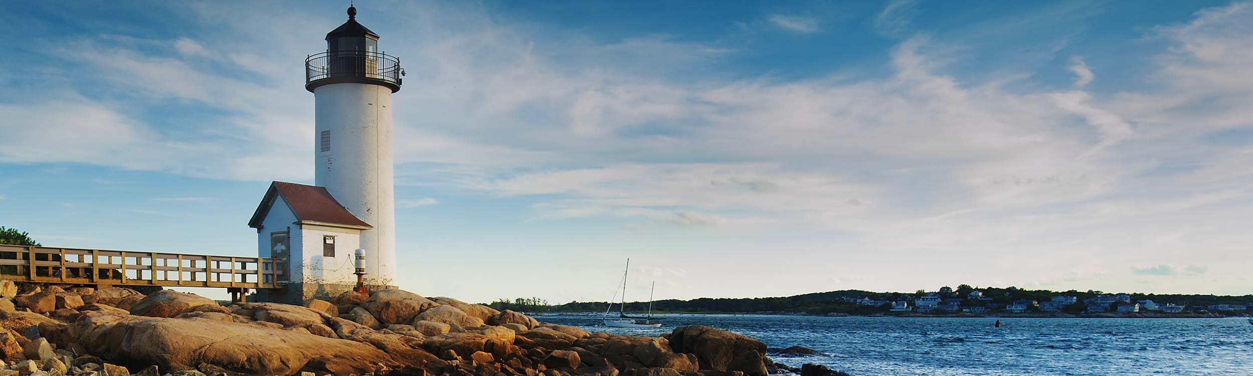 Annisquam Harbor Lighthouse with a wooden walkway on a rocky shoreline in Gloucester, Massachusetts.